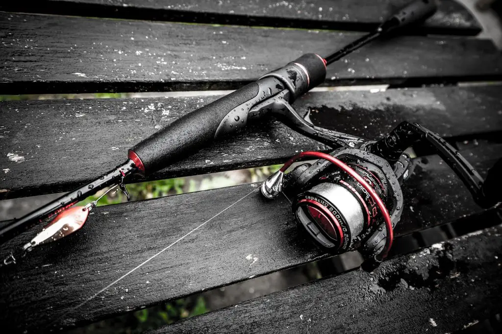 A portrait image of a wet graphite fishing rod on a bench