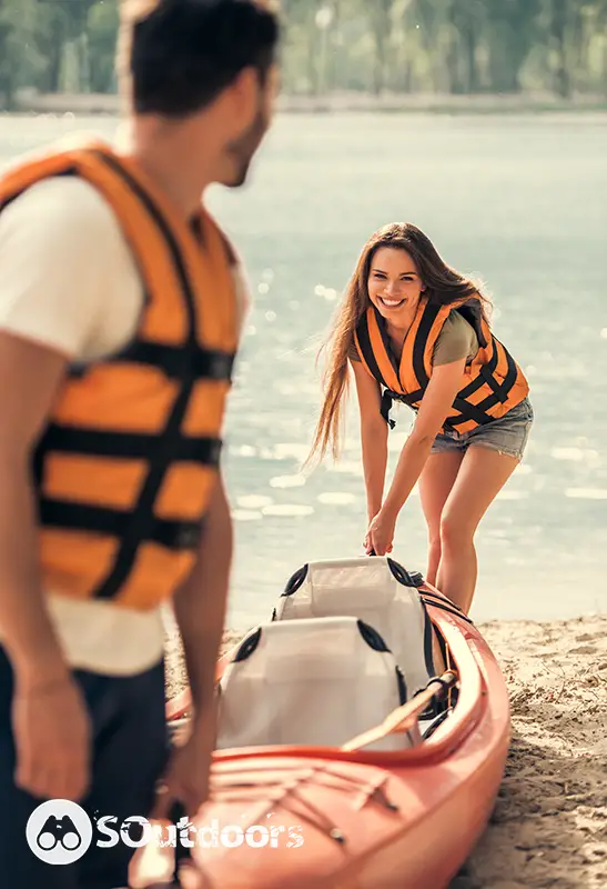 Young couple pulling a two seater kayak on the beach after sailing