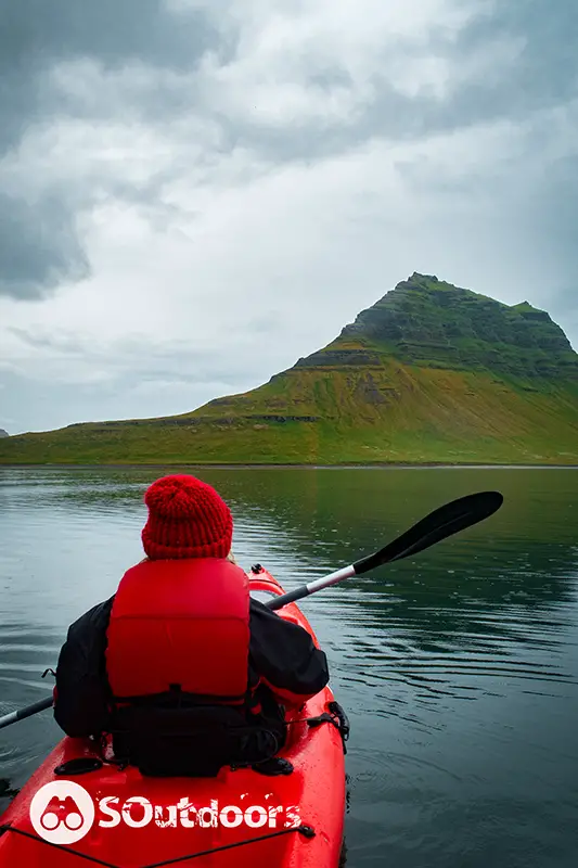 A man siting on top of a vibrant red colored kayak looking at the green mountain