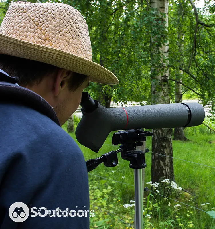 Young man wearing a straw hat is looking through the spotting scope