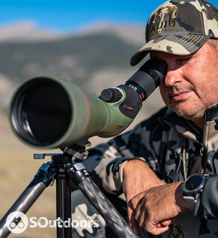 A man wearing a baseball cap looking through a spotting scope that is mounted on a tripod