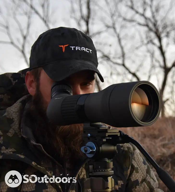 A man wearing a baseball cap looking at his spotting scope