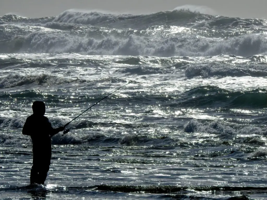 Man fishing near the sea shore with big waves on the background