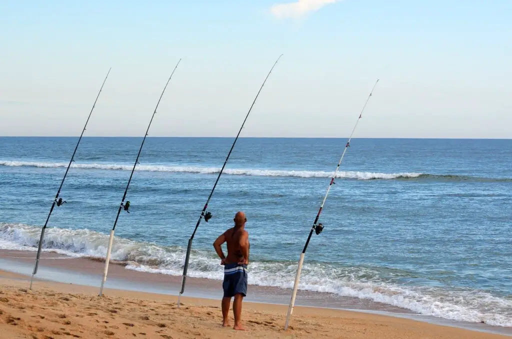A man standing by the seashore with his fishing rods mounted