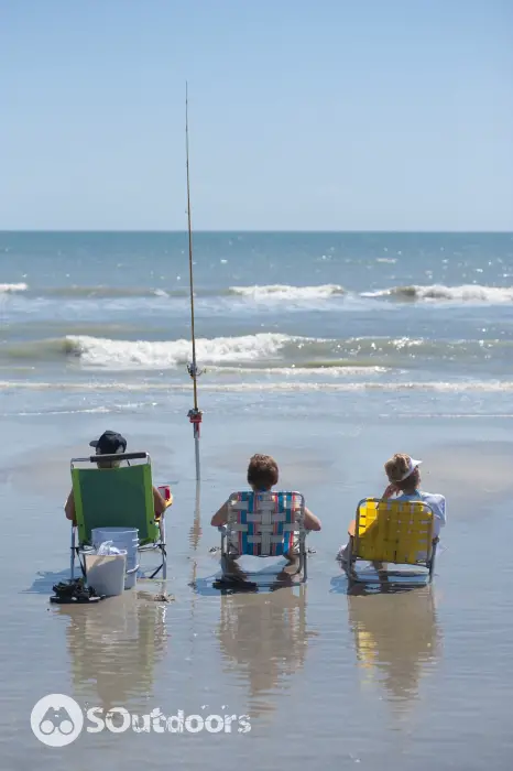 Three people surf fishing with one fishing pole