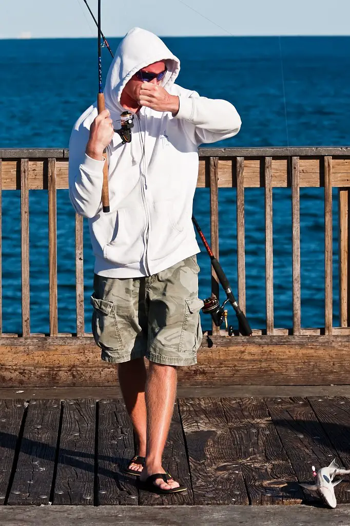 A man happily pulls out his fishing rod with a fish caught on his bait