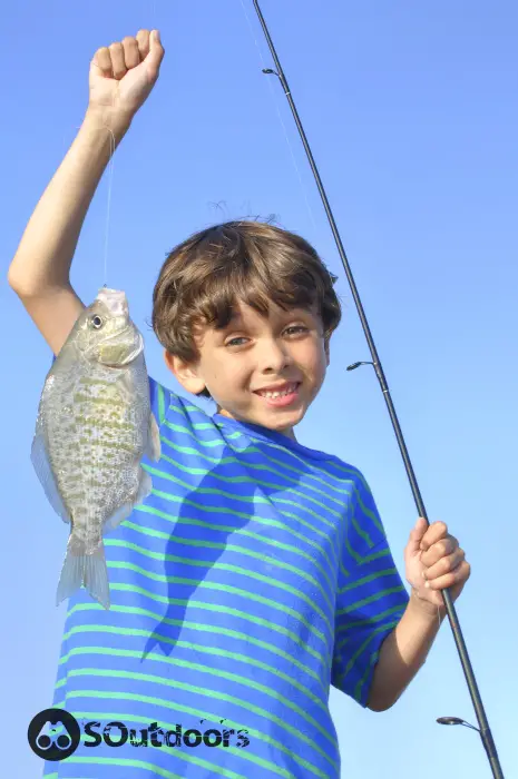 A young boy holds up a fish he caught while surf fishing in California